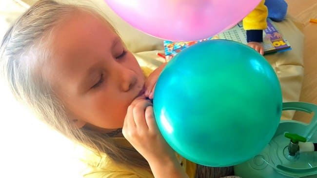 Девочка надувает воздушный шарик